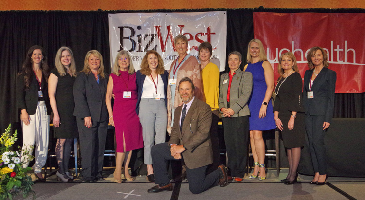 A group of women lined up on stage in front of the BizWest and UCHealth banners