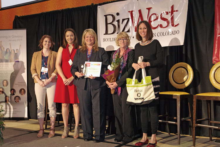A group of women holding flowers, certificates and gift bags on stage