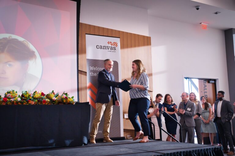 A handshake on stage beside a Canvas banner