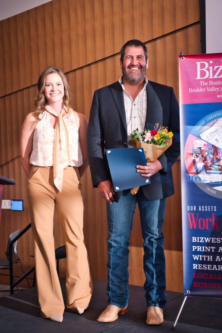A woman beside a man holding flowers and a certificate on stage