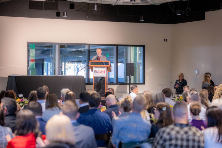 A speaker at the BizWest podium addressing a full room