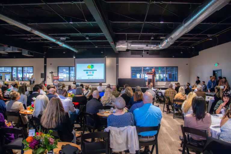 The audience seated at tables facing the stage screen