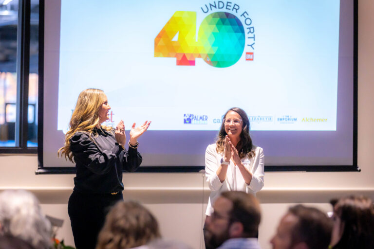 Two women applauding on stage in front of the 40 Under Forty logo