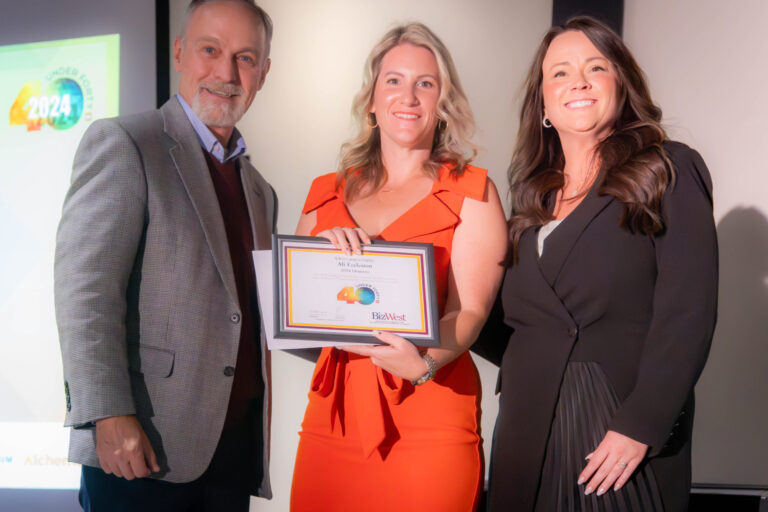 An honoree in orange holding a certificate between two presenters