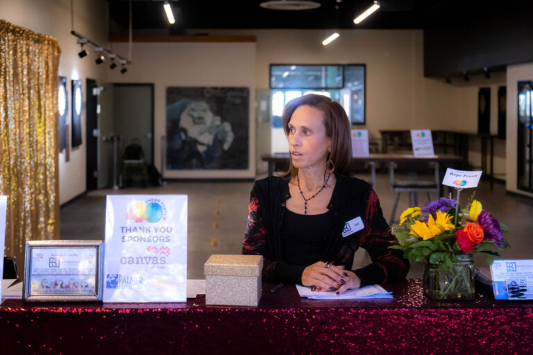 A woman seated at the check-in table beside a sponsor thank-you sign