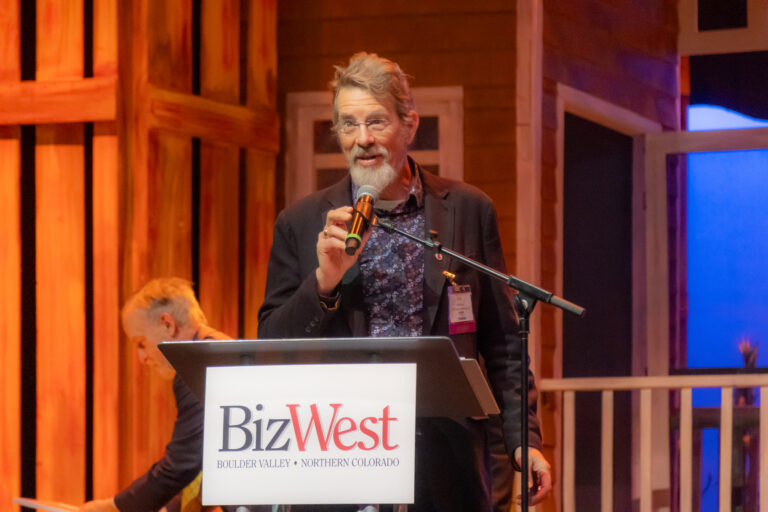 A speaker raises a glass at the BizWest podium during the 2025 program