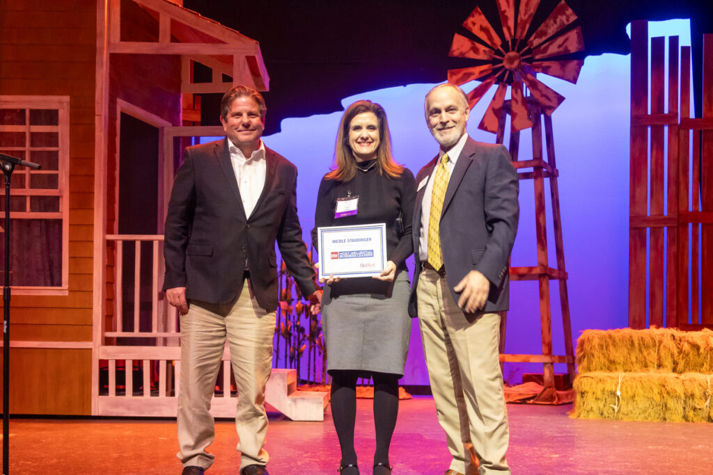 Three honorees on stage holding an award at the 2025 Most-Influential Business Leaders event (March 10, 2025, Candlelight Dinner Theater)