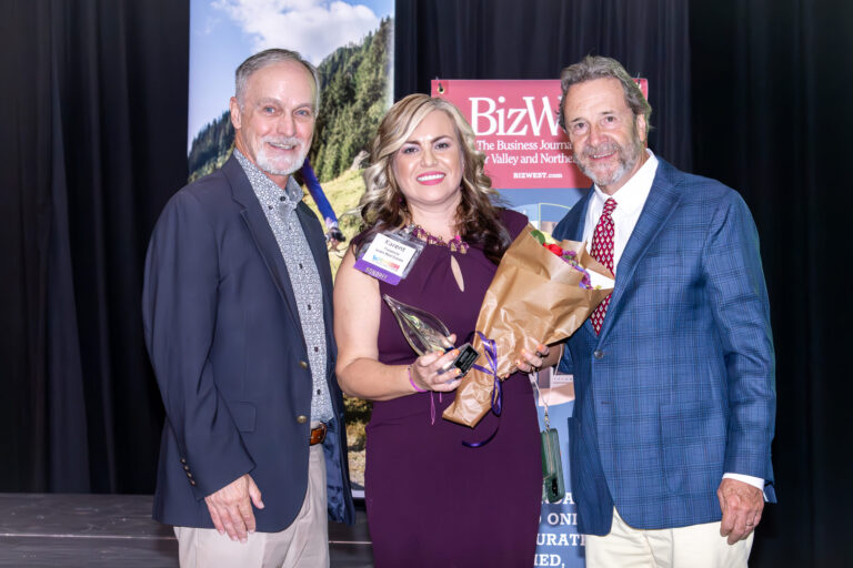 An honoree holding flowers and an award between two presenters on stage