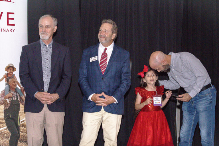 Two presenters on stage as a child in a red dress joins them