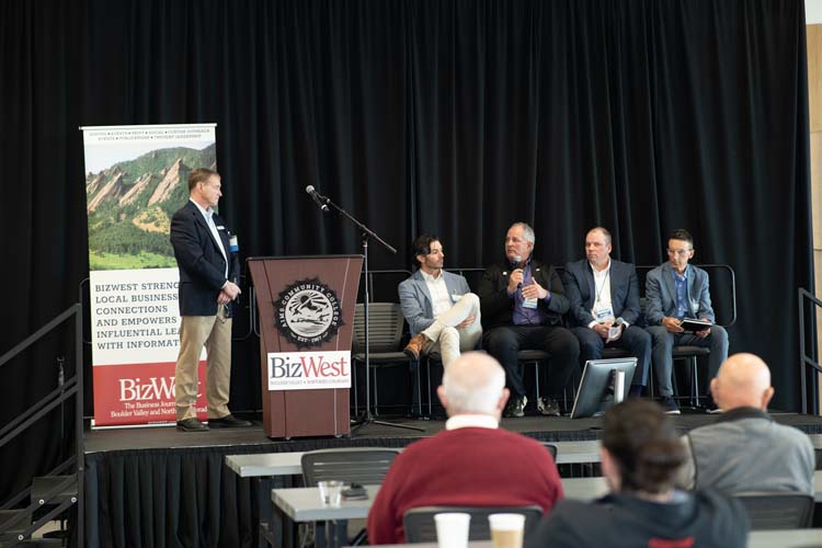 A moderator at the podium and four panelists on stage at Confluence 2026