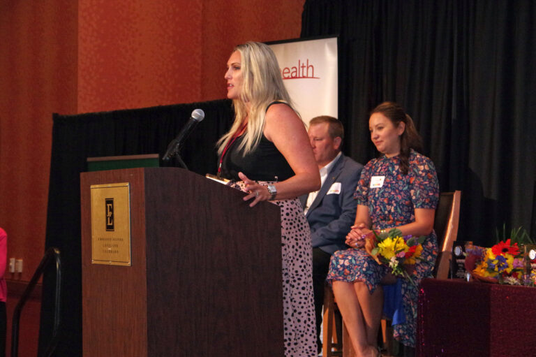 A speaker at the podium with two people seated on stage
