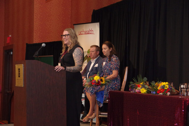 A speaker at the podium beside two people seated on stage